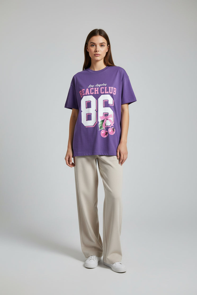 Purple t-shirt with 'Los Angeles Beach Club 86' text on a wooden surface